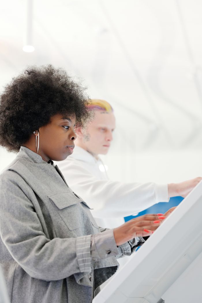 A stylish woman with afro-textured hair is seen from the side, using a touchscreen indoors.
